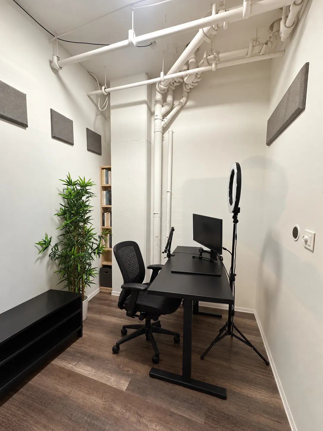 Bureau privé 104-1 au 2727 Coworking, Griffintown : bureau noir avec écran et fauteuil en filet, panneaux acoustiques gris, grande plante et tuyaux blancs apparents