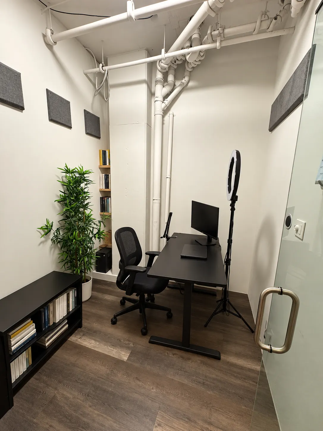 Private office 104-1 at 2727 Coworking, Griffintown: view from the glass door showing the desk, a low bookcase and a narrow book shelf in the corner