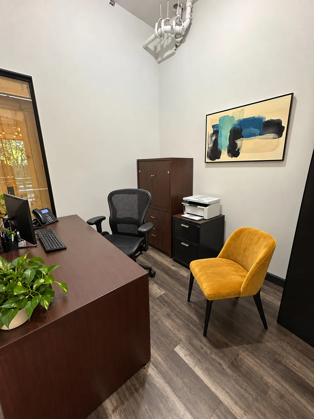 Bureau privé 105-2 au 2727 Coworking, Griffintown : bureau de direction en bois, fauteuil en filet, fauteuil en velours moutarde, armoire en bois et toile abstraite