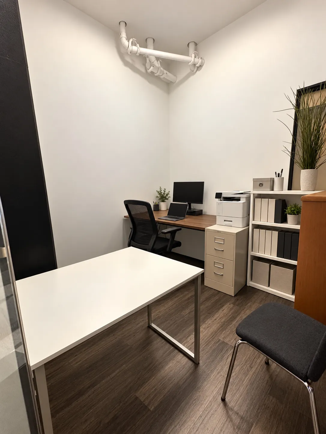 Bureau privé 105-3 au 2727 Coworking, Griffintown : table de réunion blanche avec chaise visiteur, bureau couleur noyer avec écran, classeur et étagère ouverte