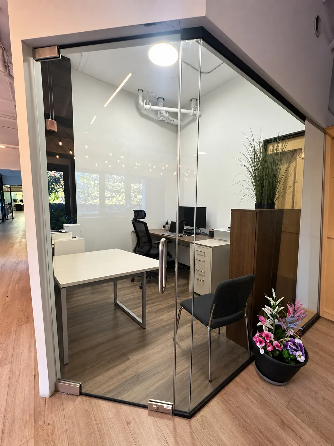 Private office 105-3 at 2727 Coworking, Griffintown: the office through its glass corner, with a tall potted grass and flowers at the door