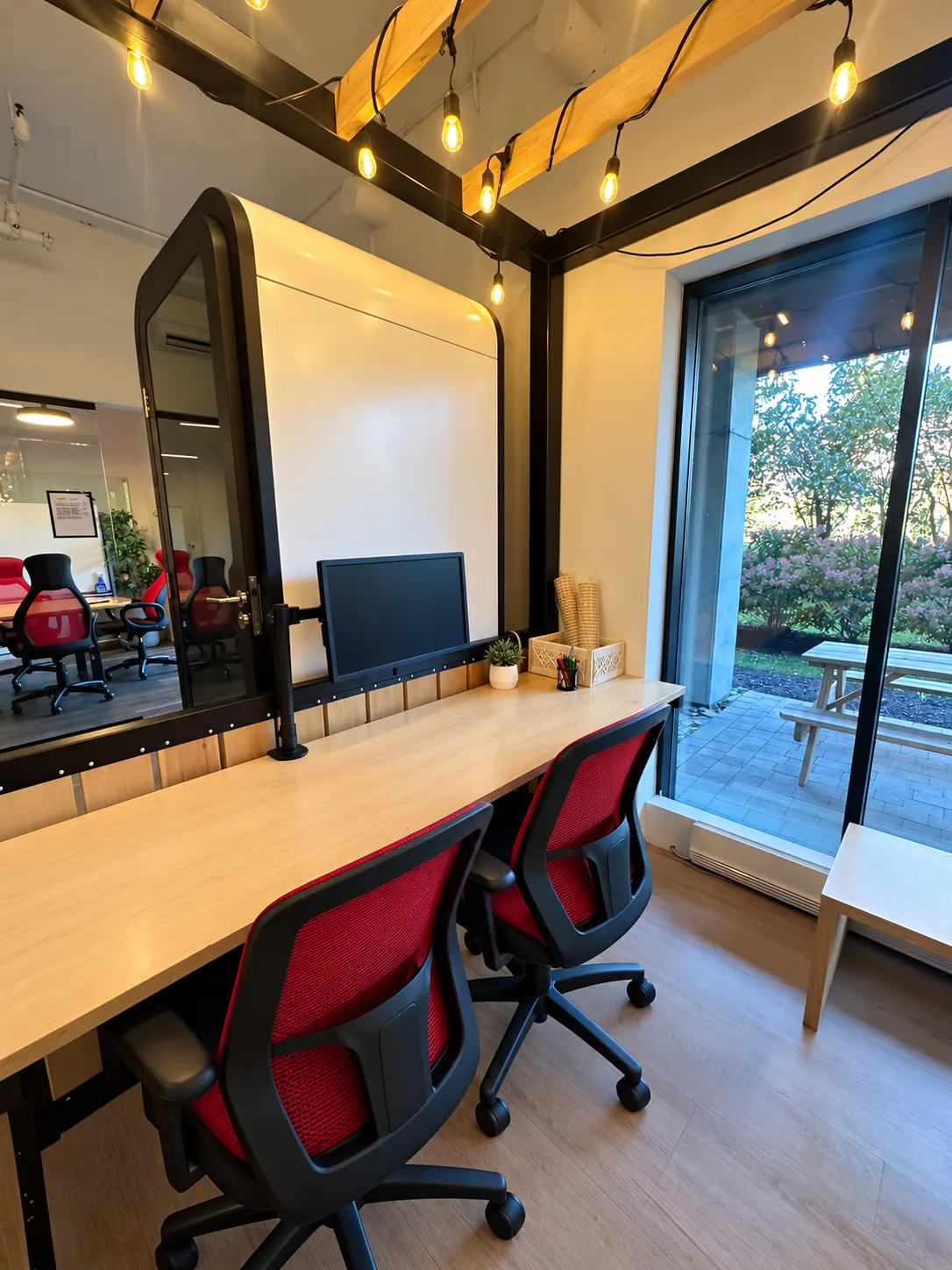 Poste dédié 105-AB au 2727 Coworking, Griffintown : long comptoir en bouleau, chaises rouges en filet, cabine téléphonique à gauche et grande fenêtre sur les arbres
