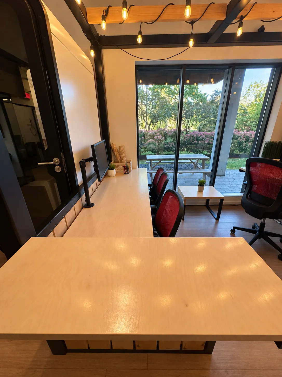 Dedicated desk 105-AB at 2727 Coworking, Griffintown: birch desktop under timber beams and string lights, looking out a floor-to-ceiling window