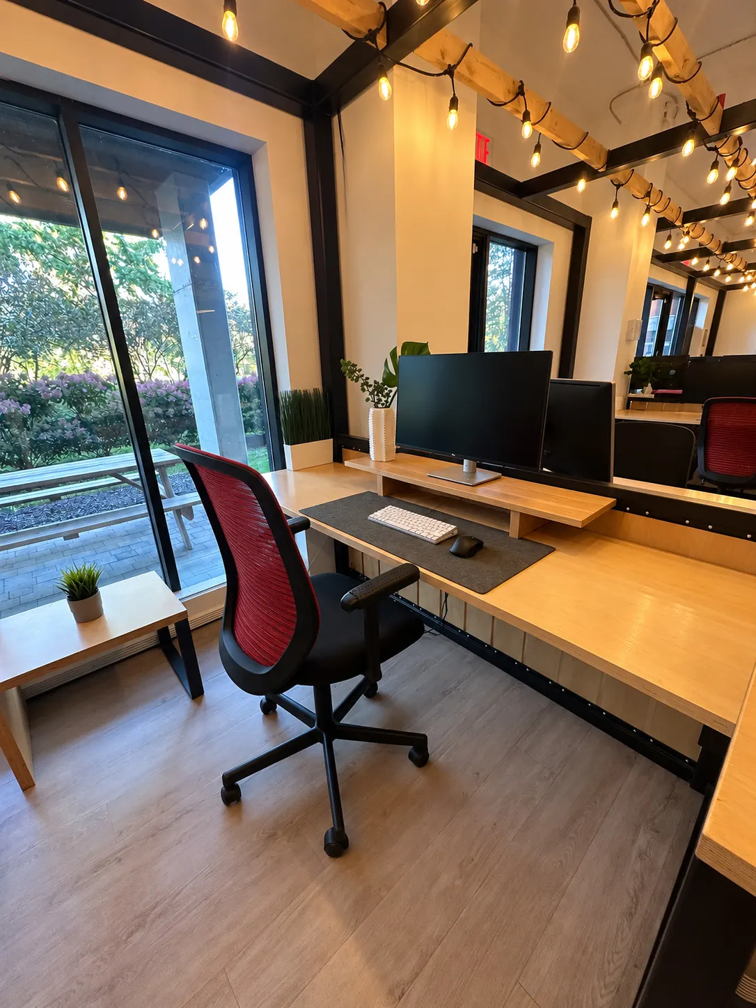 Poste dédié 105-CD au 2727 Coworking, Griffintown : bureau en bouleau avec tablette surélevée pour l'écran et chaise rouge en filet, à côté d'une grande fenêtre sur les arbres