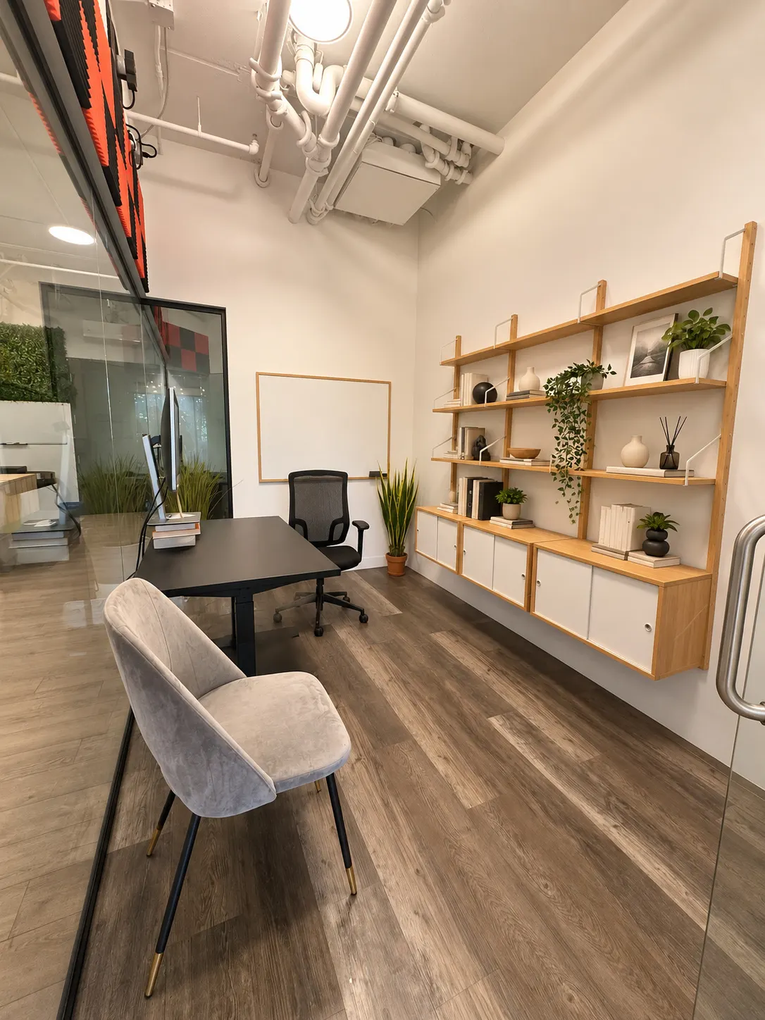 Bureau privé 106-2 au 2727 Coworking, Griffintown : pièce allongée avec mur d'étagères en chêne et blanc, bureau noir, chaise grise rembourrée et tableau blanc