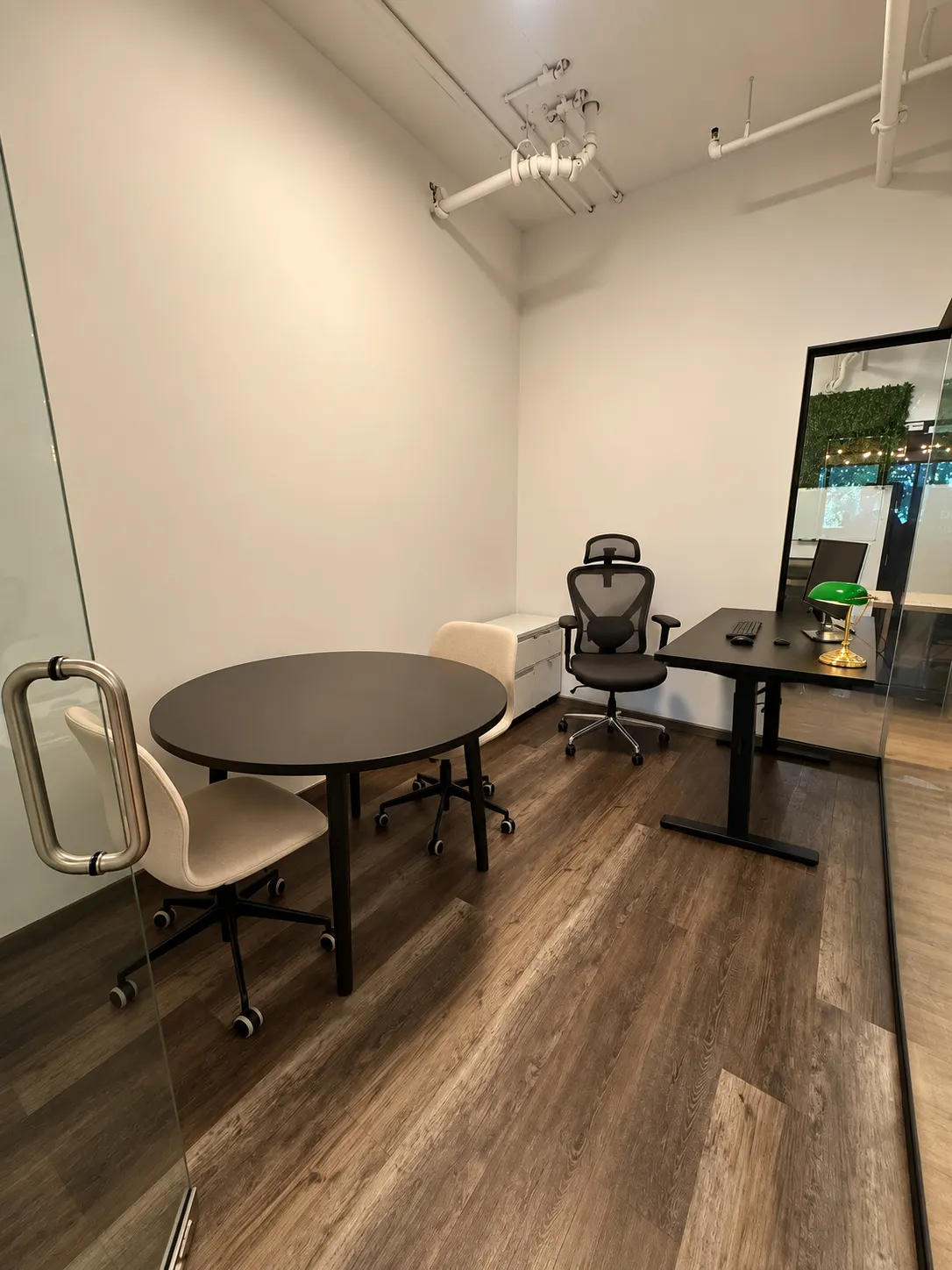 Bureau privé 106-3 au 2727 Coworking, Griffintown : table ronde noire avec deux chaises crème, et bureau noir avec lampe de banquier verte