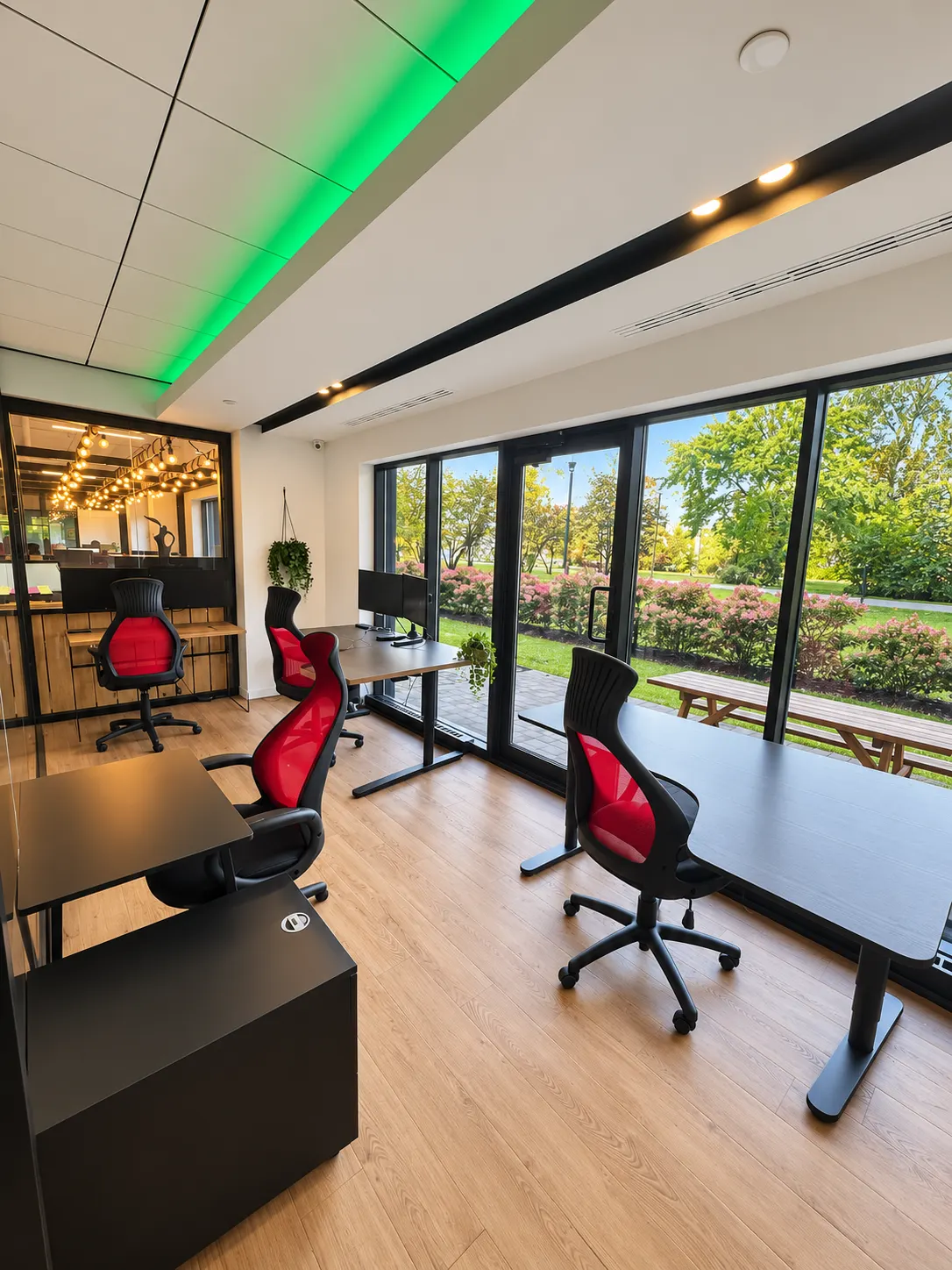 Bureau privé 107-4 au 2727 Coworking, Griffintown : bureaux foncés et chaises ergonomiques rouges devant des fenêtres pleine hauteur donnant sur des arbustes et des arbres.