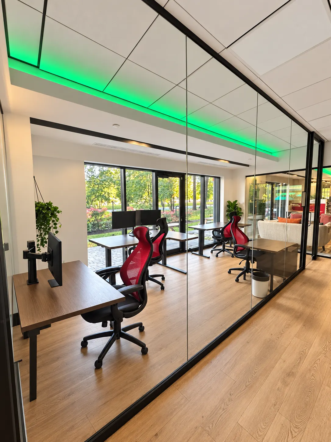 Private office 107-4 at 2727 Coworking, Griffintown: seen through its glass wall, four desks, a green cove light and the windows, with the lounge next door.