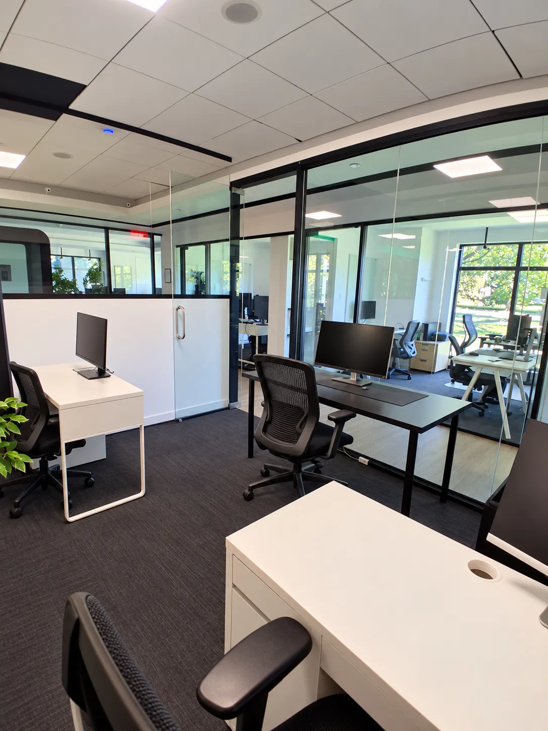 Bureau privé 109-6 au 2727 Coworking, Griffintown : bureaux blancs et noirs entre des murs vitrés à cadre noir, avec des fenêtres visibles de l'autre côté de l'étage.