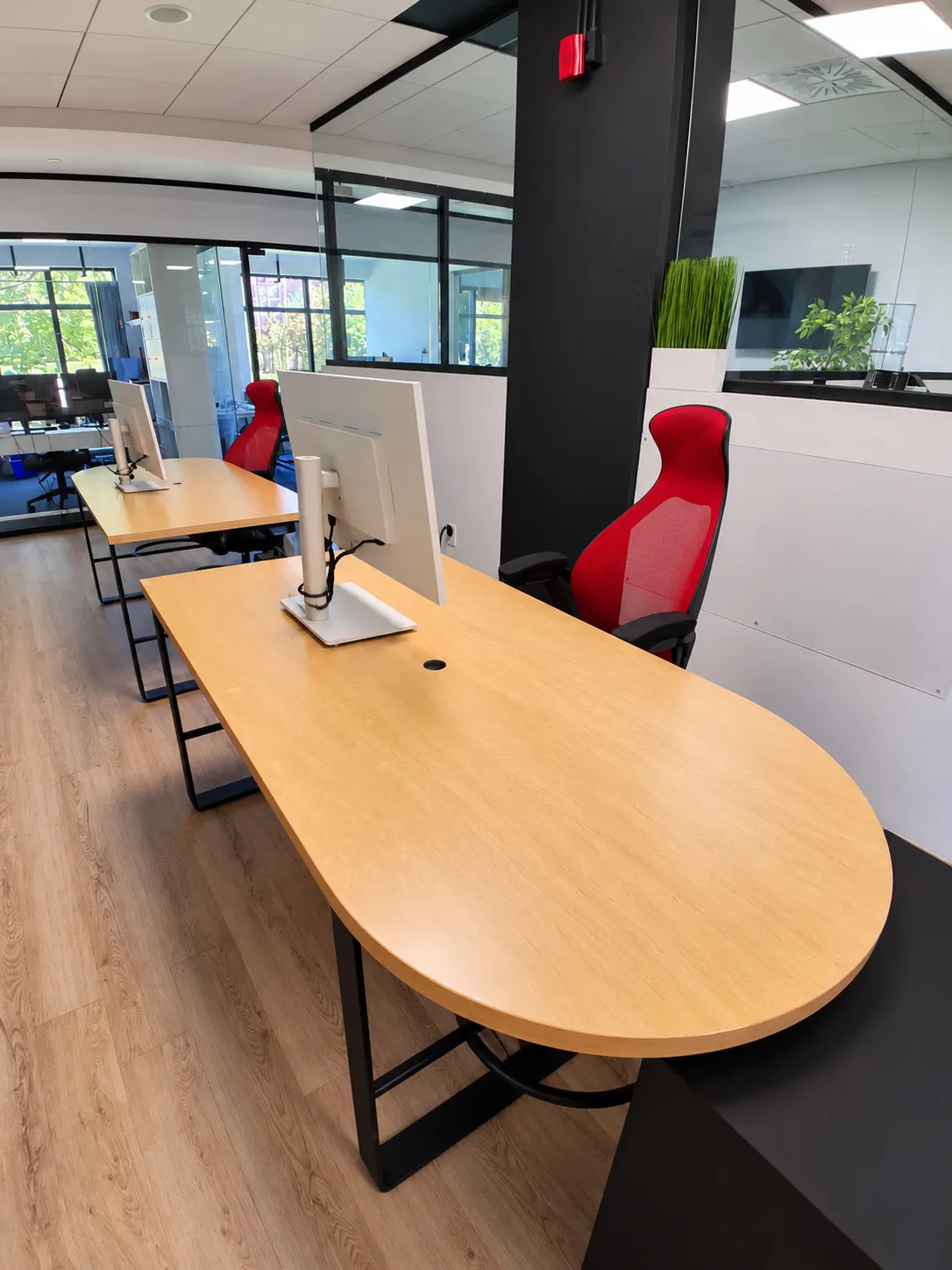 Poste dédié 109-B au 2727 Coworking, Griffintown : bureau arrondi en chêne et chaise rouge à dossier haut dans une aire ouverte lumineuse, à côté de bureaux vitrés