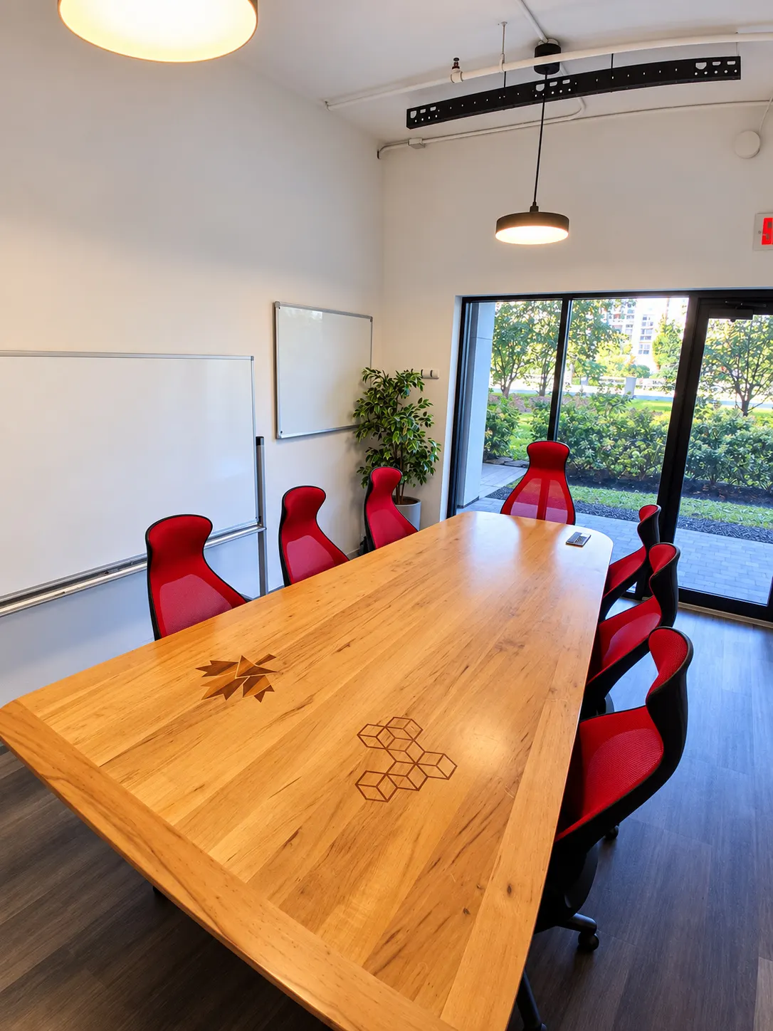 Salle de conférence du 2727 Coworking, Griffintown : table en bois marqueté, chaises rouges, deux tableaux blancs et portes vitrées sur la verdure