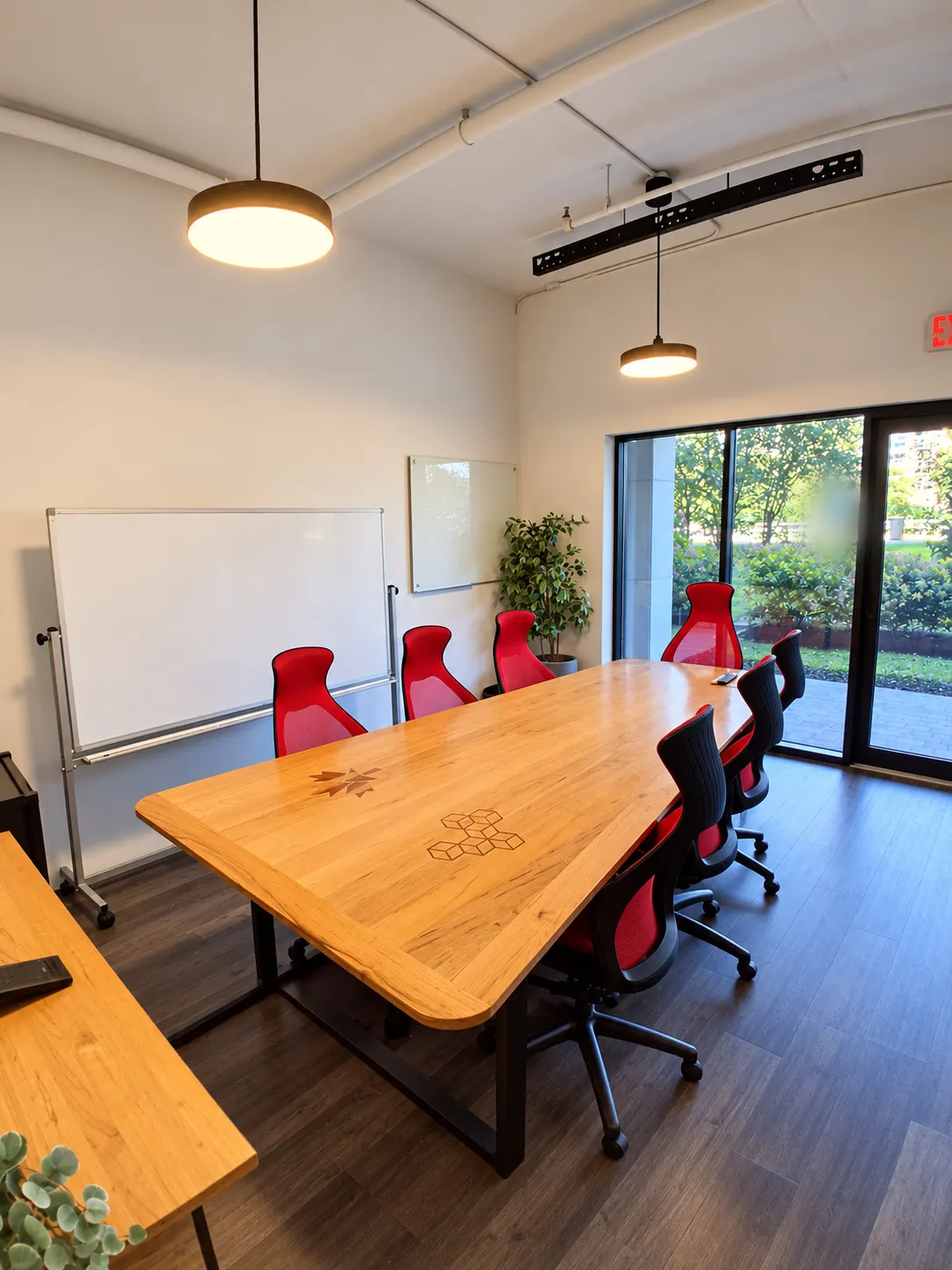 Salle de conférence du 2727 Coworking, Griffintown : chaises rouges autour d'une table en bois marqueté, luminaires suspendus et porte vitrée vers l'extérieur