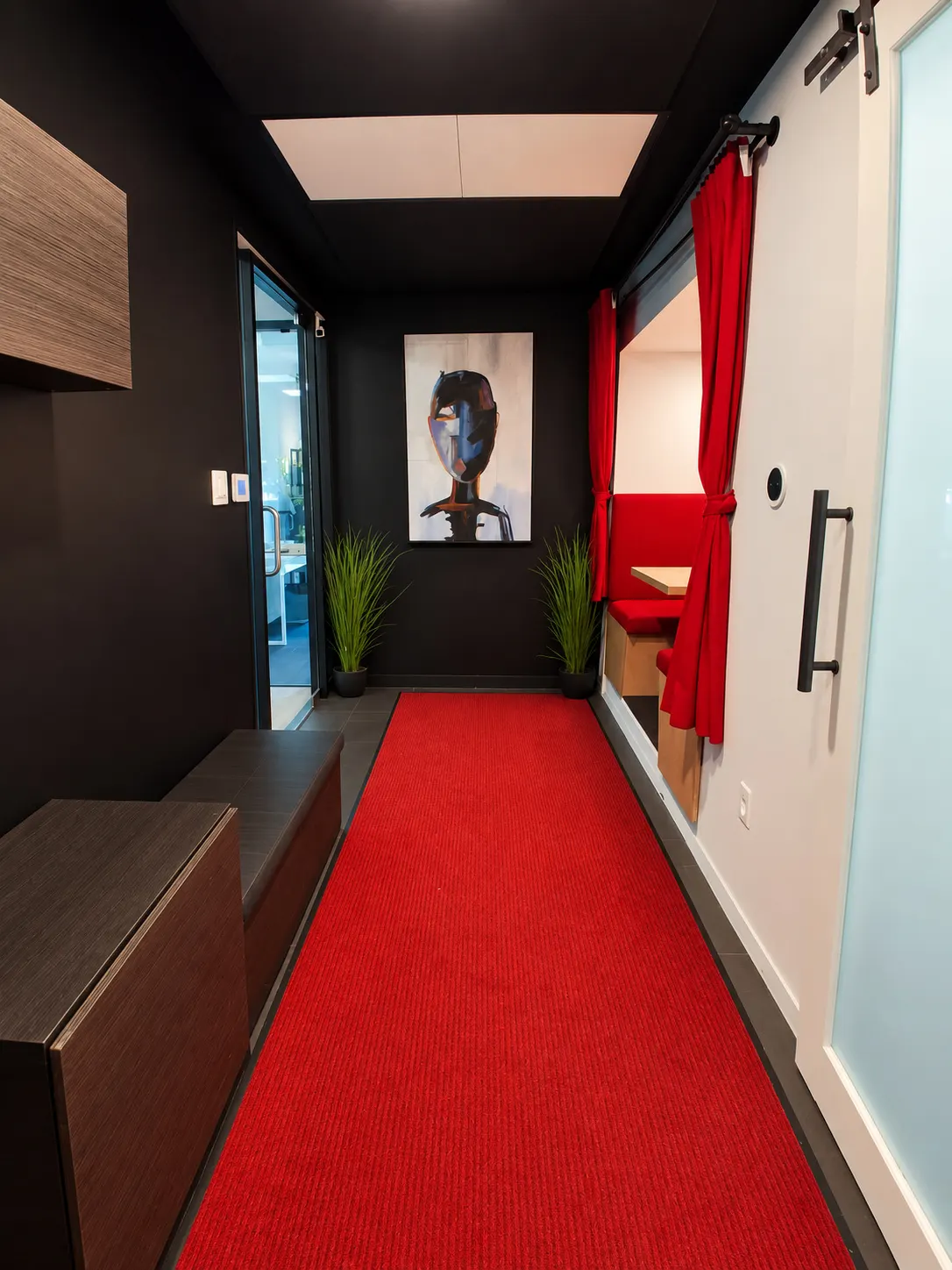 Corridor d'entrée du 2727 Coworking, Griffintown : tapis rouge, murs noirs, toile d'un portrait et alcôve à rideaux