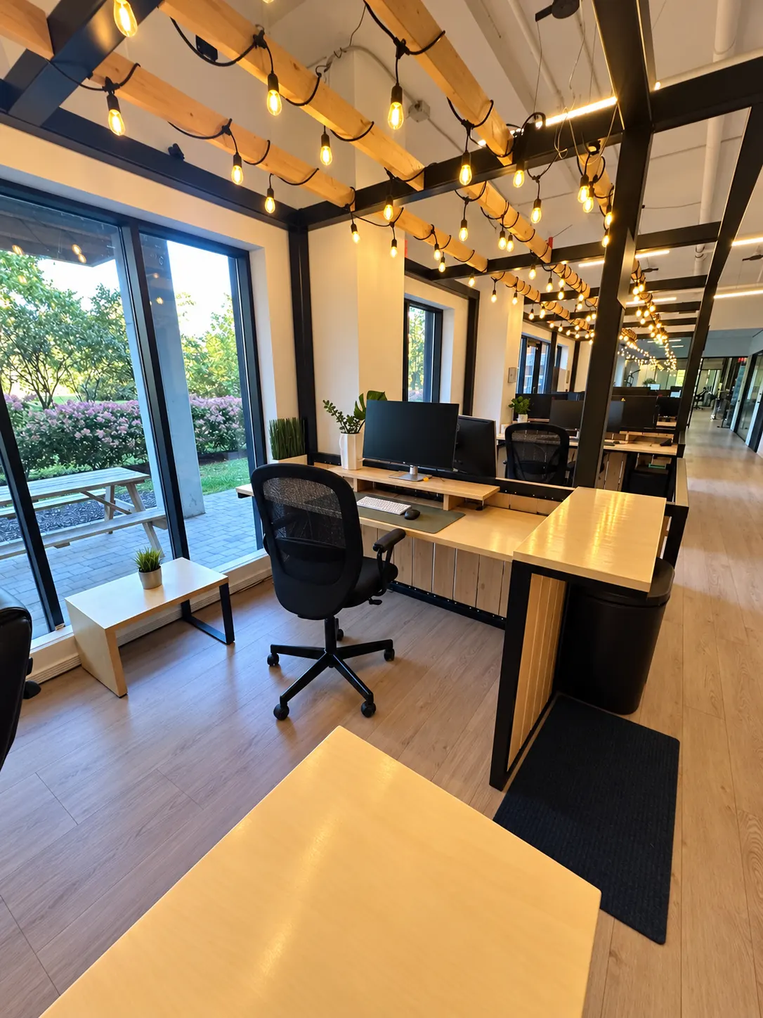 Espace de travail côté fenêtres au 2727 Coworking, Griffintown : rangée de bureaux le long de grandes fenêtres, sous des poutres de bois et des guirlandes