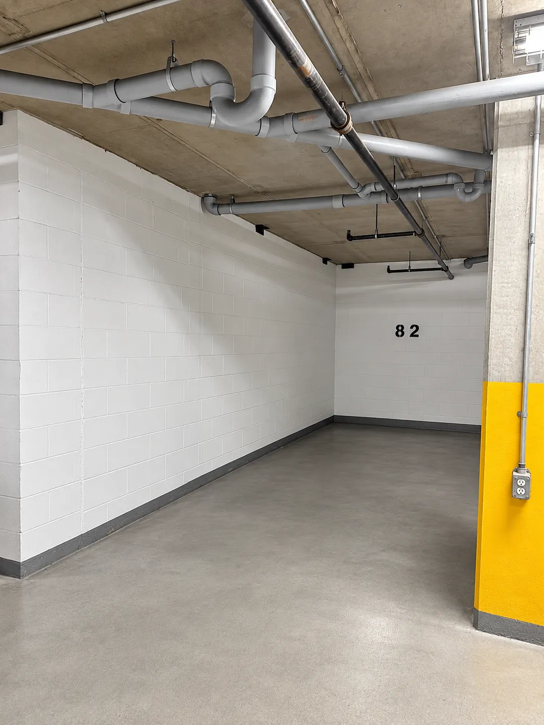 Place de stationnement 82 au 2727 Coworking, Griffintown : un emplacement intérieur profond entre des murs de blocs blancs, le numéro 82 peint sur le mur du fond et un pilier jaune à l'entrée